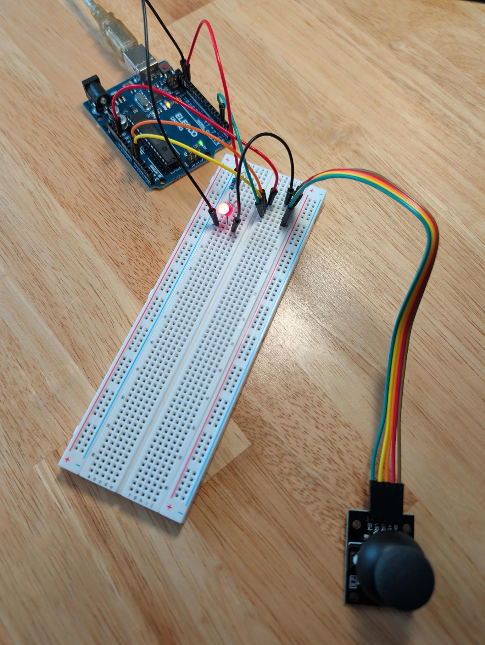 The finished circuit on the bench: an ELEGOO UNO R3 wired into a breadboard with the part-one LED glowing red, and a KY-023 joystick module off to the right, connected by a five-wire ribbon.