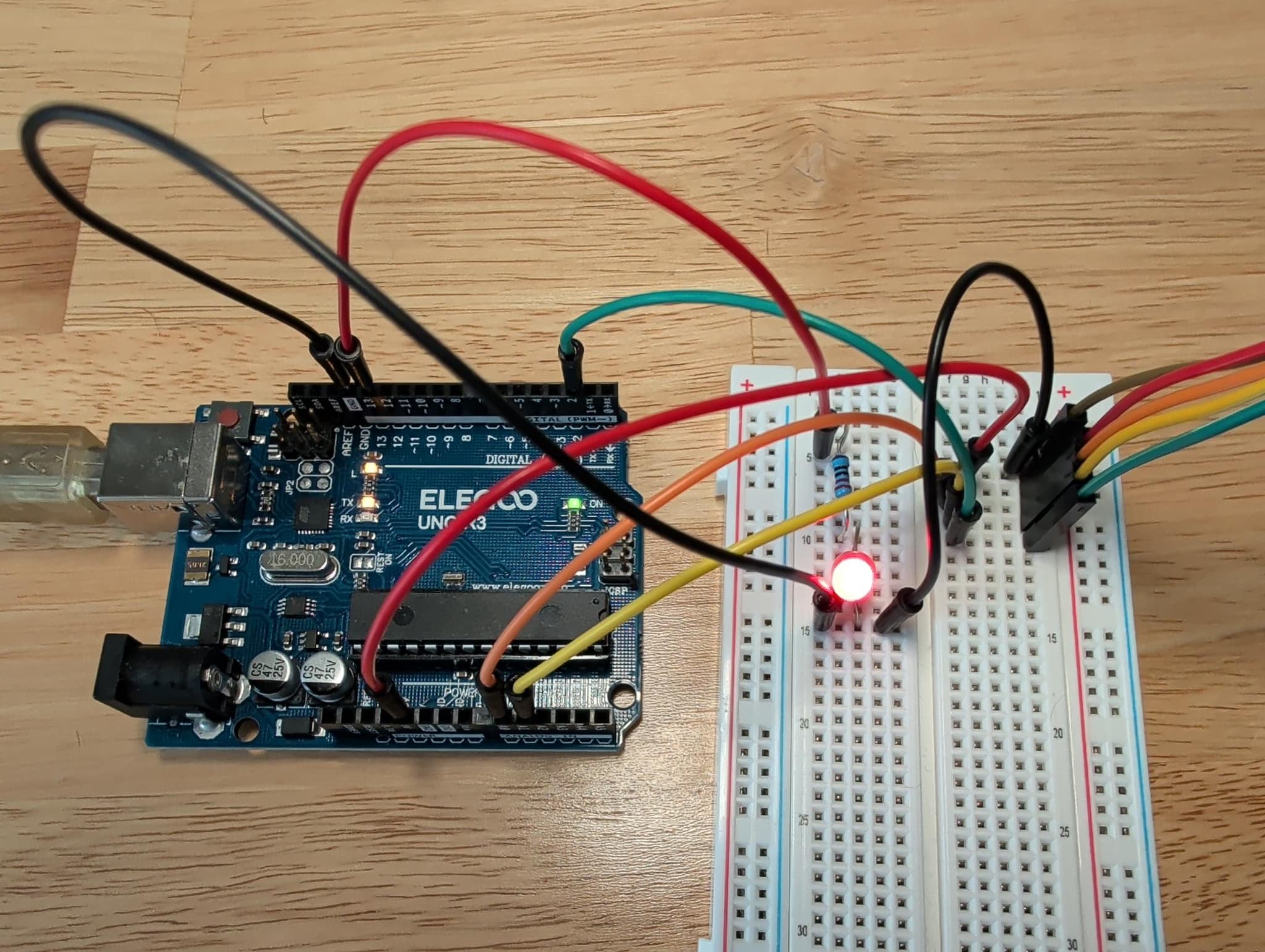 The ELEGOO UNO's jumpers running down into the breadboard with the red LED lit, and the joystick's five colored leads — red, orange, yellow, green, and black — heading off the bottom edge of the board.
